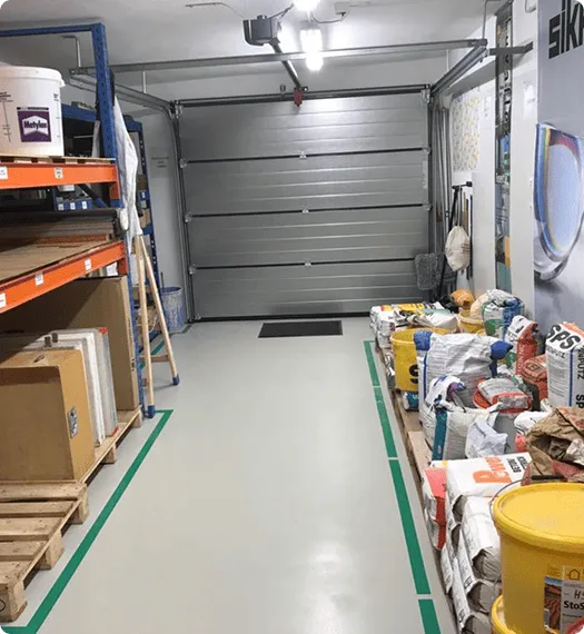 Saubere, frisch beschichtete Werkstattbodenfläche mit Regalen, auf denen Baumaterialien und Werkzeuge gelagert sind.