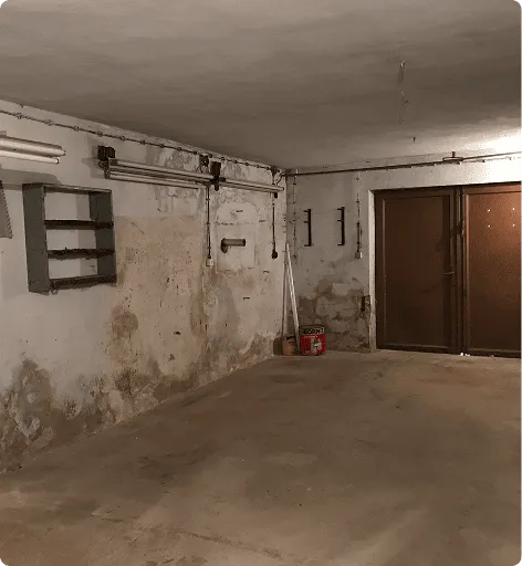 Verlassener Kellerraum mit schmutzigen Wänden, Rohren, einem Regalsystem und einer braunen Doppeltür.