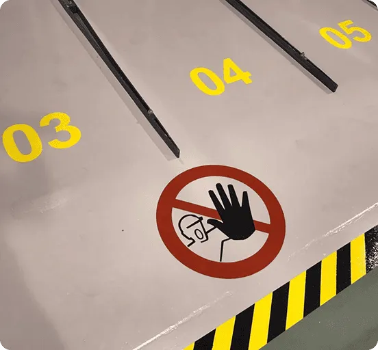 Boden mit gelben Nummern 03, 04 und 05, rotem Verbotsschild mit schwarzer Hand und Schutzhelm-Symbol sowie gelb-schwarzer Warnmarkierung am Rand.