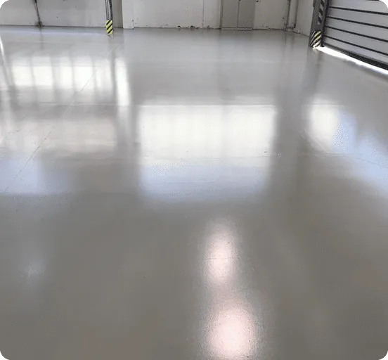 Sauberer, glänzender, hellgrauer Industrie- oder Garagenboden mit Spiegelungen von Fenstern.