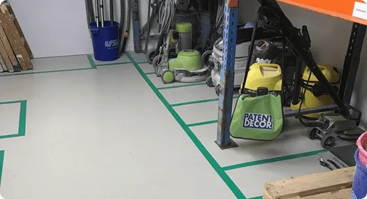 Sauberer Boden in einer Werkstatt mit grün markierten Bereichen und verschiedenen Werkzeugen und Geräten an der Wand.