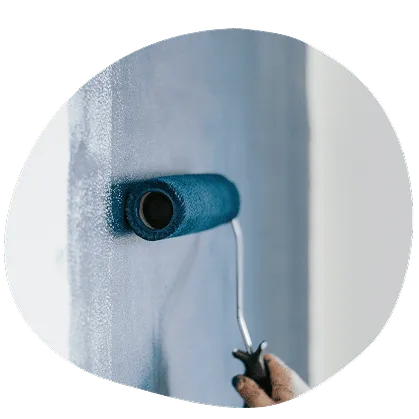 Hand hält Farbroller, der eine Wand in einem hellblauen Farbton streicht.