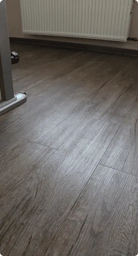 Dunkler Designbelag mit Holzmaserung auf dem Boden eines Raumes mit Heizkörper an der Wand.