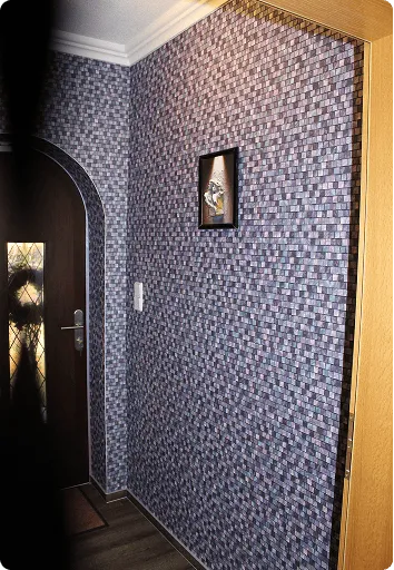 Eingangsbereich mit dunkler Holztür und Wänden, die mit grauer, geometrischer Muster-Tapete verkleidet sind, sowie einem kleinen gerahmten Bild an der Wand.