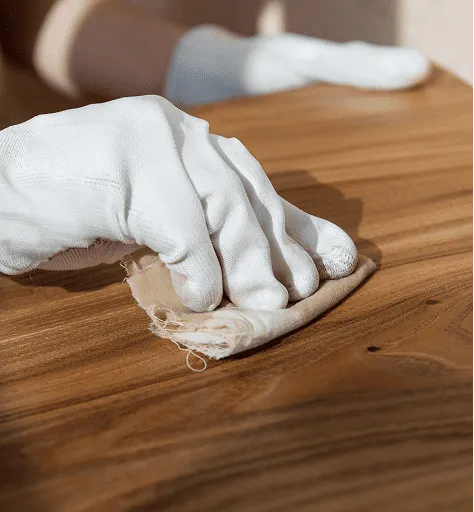 Hand in weißem Handschuh poliert eine Holzoberfläche mit einem Tuch.