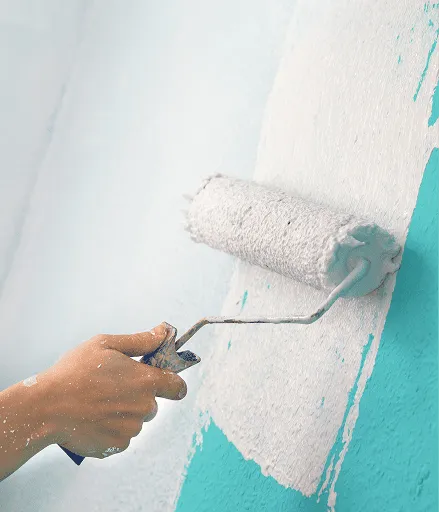 Hand mit Farbrolle trägt weiße Farbe auf eine türkisfarbene Wand auf.